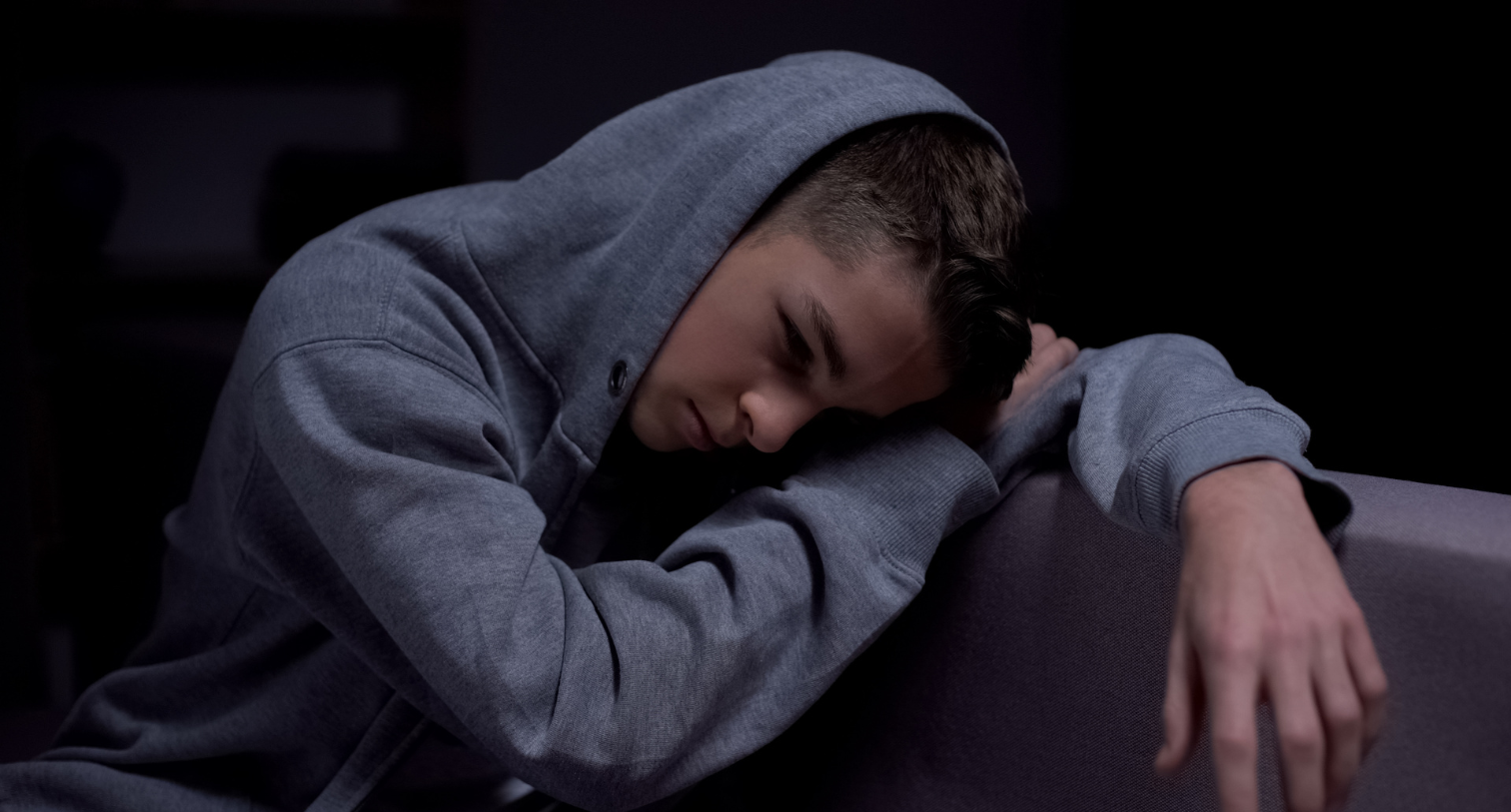 Teenage boy with a hoodie sitting down and looking sad