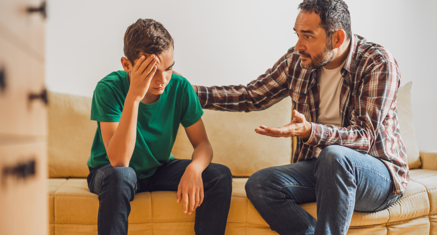 Father and son talking at home and dad is consoling his teenage son.