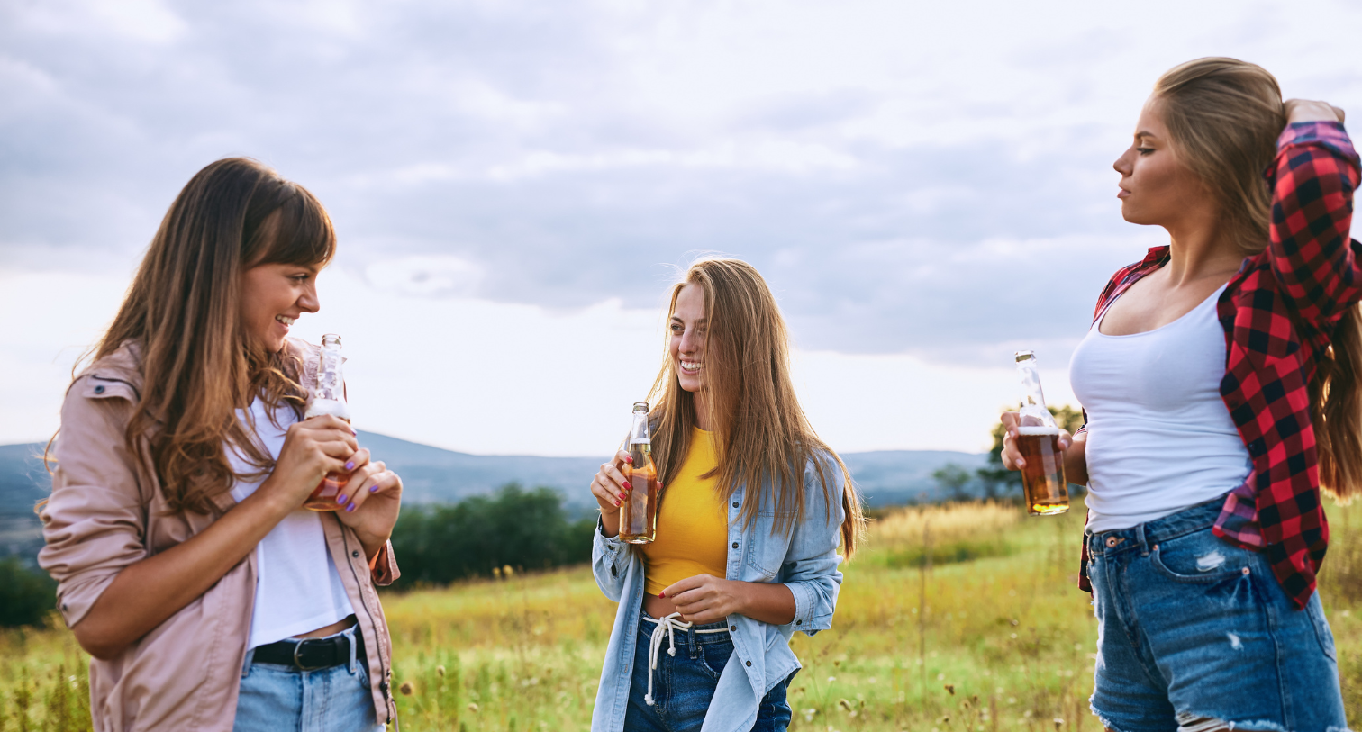 Three teenage girls drinking alcohol in a field and laughing and talking with each other