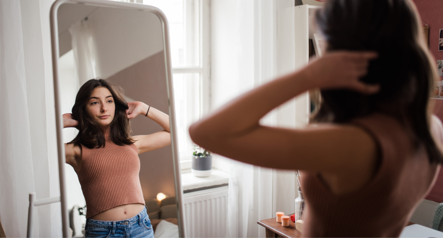 Young teenage girl looking in the mirror in her room.