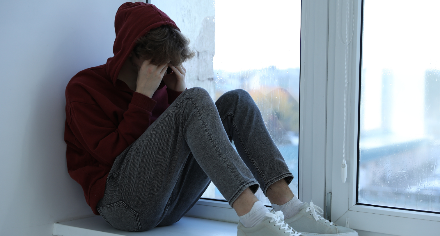 Depressed teenage boy near window at home