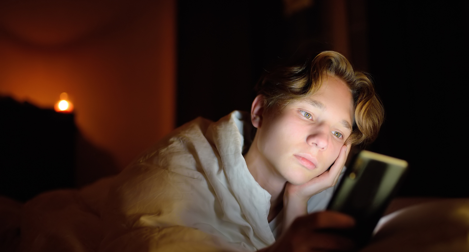 Teenage boy in a dark room looking at the smartphone with reflective light