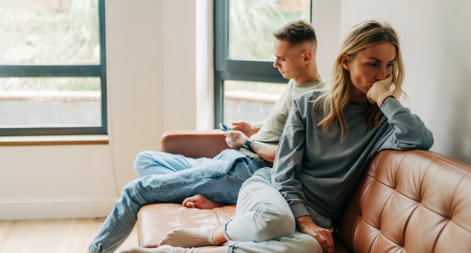 Woman looking sad and unhappy sitting on sofa with her male partner who is looking at his phone