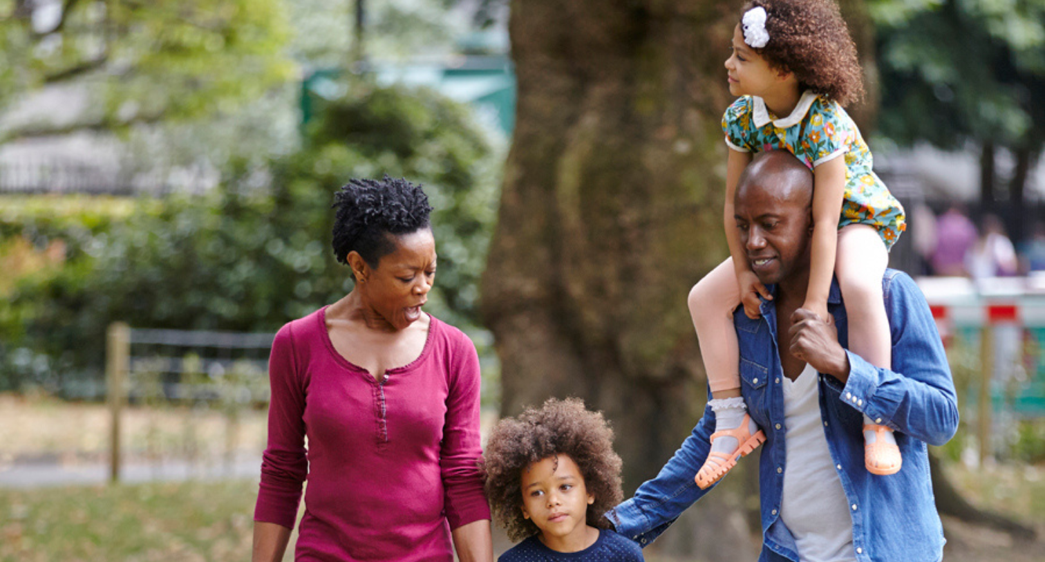 Mum, dad and son and daughter walking through the park with daughter on dads shoulders