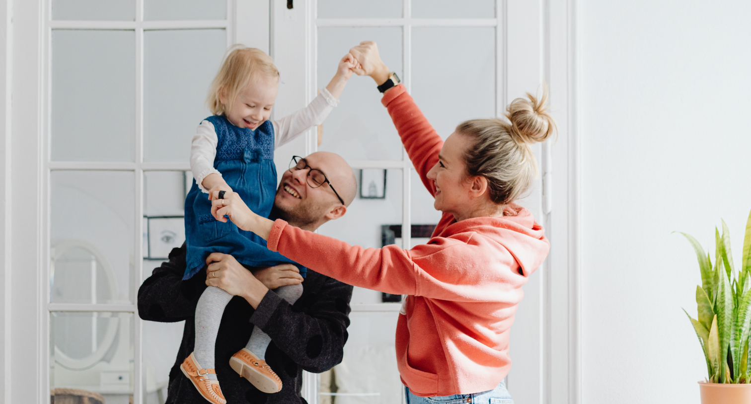 Mum and dad playing with their toddler daughter with arms waving in the air