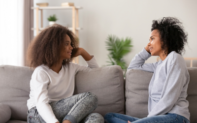 Mum and teenage daughter sitting on sofa talking to each other in deep conversation