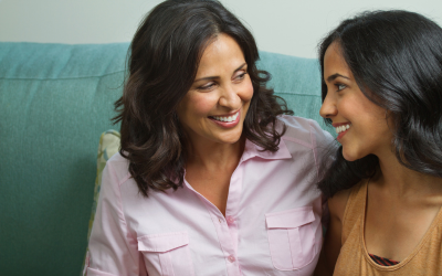 Mother and teen daughter smiling at each other whilst sitting on the sofa