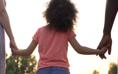 A young girl holding hands with her parents walking outside