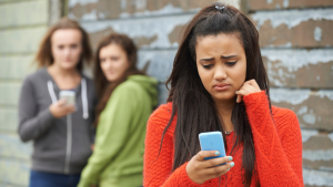 girl being bullied online with girls behind her being mean